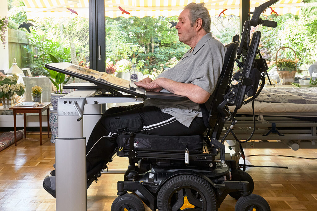 Wheelchair user working at a Ropox height adjustable desk with tilting tabletop